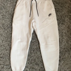 Vita mjukisbyxor från Nike - Säljer ett par vita mjukisbyxor från Nike i storlek M. Byxorna har dragsko i midjan, fickor på sidorna och en svart Nike-logga framtill. Perfekta för en avslappnad stil och riktigt sköna att ha på sig.