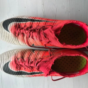 Röda Nike fotbollsskor med snörning - Säljer ett par vit rosa Nike mercurial superfly acc där strumpan är klippt i storlek 44 är i bra skick o andvända ett fåtal gånger