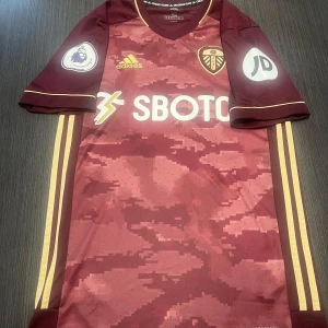 Äkta Leeds tröja men premier league patches  - Säljer min vackra Leeds United tröja i storlek xs! Tröjan är i nyskick förutom att märket på bröstet har släppt lite, men knappt använd med sbotop sponsor på magen! Produktkoden är (FI6183)!  Hör gärna av dig vid minsta lilla fundering och kolla gärna in mina andra produkter på min profil!     Fotboll fotbollströja fotbollsskor Nike Barcelona T-shirt grisch thiago alcantara Adidas football shirt Champions league, Europa confrence premier league patches