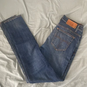 Blå jeans från Tiger of Sweden - Snygga blå jeans från Tiger of Sweden med klassisk femficksdesign och raka ben. Jeansen har orangea kontrastsömmar och läderpatch bak i midjan. Perfekta för dig som gillar stilrena och tidlösa jeans. Fråga vid minsta lilla fundering!
