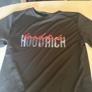 Svart t-shirt från Hoodrich - Snygg svart t-shirt från Hoodrich med ett coolt tryck i vitt och rött på framsidan. Perfekt för en avslappnad stil.