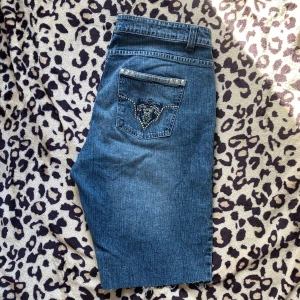 Jeansshorts - Snygga jeansshorts med coola nitar och broderi på fickorna. Perfekta för en avslappnad stil med en touch av bling. De har en klassisk blå jeansfärg och är designade med en bekväm passform.
