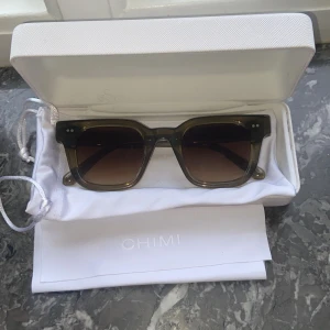 Gröna solglasögon från CHIMI - Snygga solglasögon från CHIMI med fyrkantig form . Glasen är tonade i brunt och bågarna har en stilren design med två små silverdetaljer framtill. Perfekt accessoar för soliga dagar.