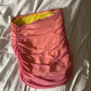 Rosa och gul  kjol  - Säljer en kjol  kort i rosa och gul med draperad omlott-design. Kjolen har en snygg rynkad effekt framtill och är fodrad med gult tyg på insidan. Perfekt för sommarens alla tillfällen!