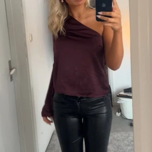 Vinröd oneshoulder topp - Säljer en vinröd oneshoulder topp med lång ärm på ena sidan. Toppen har en snygg drapering vid halsen och är tillverkad i ett mjukt, glansigt material. Perfekt för dig som vill sticka ut med en trendig och elegant look. Tröjan är ej smutsig utan d är smuts på spegeln❤️