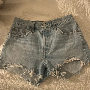 Ljusa jeansshorts från Levi's - Säljer ett par ljusa jeansshorts från Levi's med fransiga kanter och klassisk femficksdesign. Köpta på plick men inte kommit till användning då dem var för stora för mig. Vet inte riktigt vilken storlek dem är i men har för mig att dem var i w28.☺️