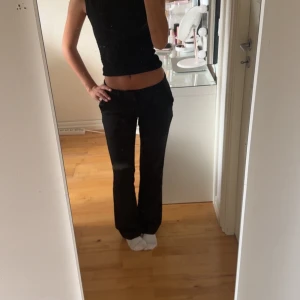 Svarta bootcut byxor - Säljer ett par svarta bootcut kostymbyxor med låg midja. Byxorna har en klassisk passform och är perfekta för en stilren look. Materialet känns mjukt och följsamt, och de har en enkel design utan synliga detaljer.
