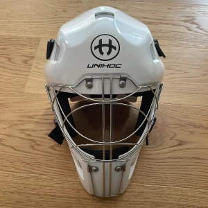 Vit innebandymålvaktshjälm - Säljer en vit innebandymålvaktshjälm från Unihoc med svart logga framtill. Hjälmen har ett robust galler i metall, justerbara svarta remmar och vaddering på insidan för extra komfort. Köpte hjälmen 2022 men den användes bara ett fåtal gånger. Nypris: 1600kr Mitt pris: 500kr