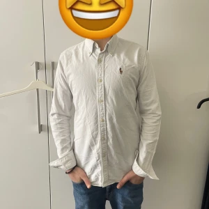 Vit långärmad skjorta från Ralph Lauren - Slim Fit✅Säljer en klassisk vit långärmad skjorta från Ralph Lauren med broderad logga på bröstet. Skjortan har knappar framtill och en stilren design som passar till många tillfällen.