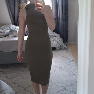 Ärmlös långklänning i ribbat tyg. Ny. - Grön ärmlös klänning med hög krage. Klänningen har en tight passform men är väldigt stretchig. Passar uppskattningsvis S-M