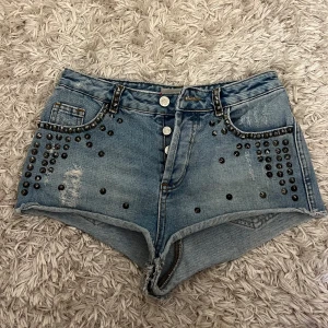 Jeansshorts med nitar från Moto - Snygga ljusblå jeansshorts från Moto med nitar framtill och slitna detaljer. Modellen är kort och har råa kanter nertill. Perfekta för sommaren och ger en cool vibe till outfiten.