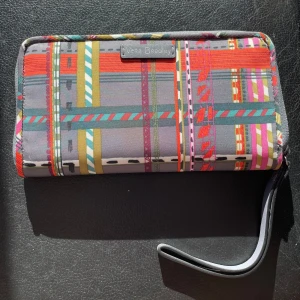 Färgglad plånbok från Vera Bradley - Säljer en färgglad plånbok från Vera Bradley med ett rutigt mönster i flera färger. Plånboken har en praktisk dragkedja och flera fack inuti för kort och kontanter. Perfekt för att hålla ordning på dina tillhörigheter med stil!