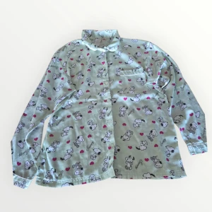 Mönstrad pyjamas med Snoopy 170 - Säljer en cool långärmad pyjamaa med Snoopy-motiv och små rosa hjärtan. Skjortan är tillverkad i polyester och har en bröstficka. Perfekt för den som älskar unika och lekfulla plagg!