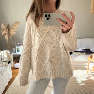 Beige stickad tröja - Mysig beige stickad tröja med ett diskret diamantmönster. Tröjan har långa ärmar och ribbade kanter som ger en klassisk look. Perfekt för kyligare dagar.