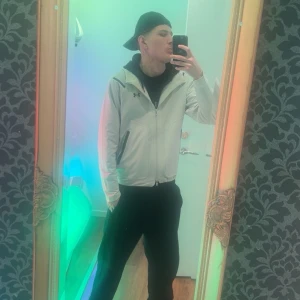 Beige/vit vindjacka från Under Armour - Säljer en stilren vit vindjacka från Under Armour. Jackan har dragkedja framtill och en diskret logga på bröstet. Perfekt för träning eller en casual look. 🏃‍♂️