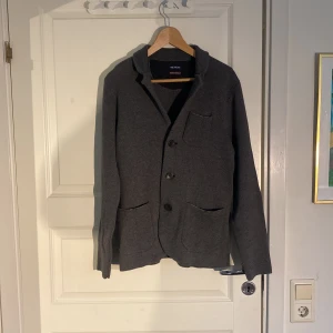 Cardigan - Säljer en grå stickad cardigan, med kavaj liknande design. Plagget är i bra skick utan defekter. Storlek small.