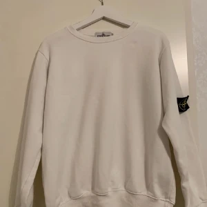 Vit tröja från Stone Island - Säljer en stilren vit tröja från Stone Island med rund hals och långa ärmar. Tröjan har en klassisk design med en diskret logga på ärmen. Perfekt för en avslappnad och trendig look.