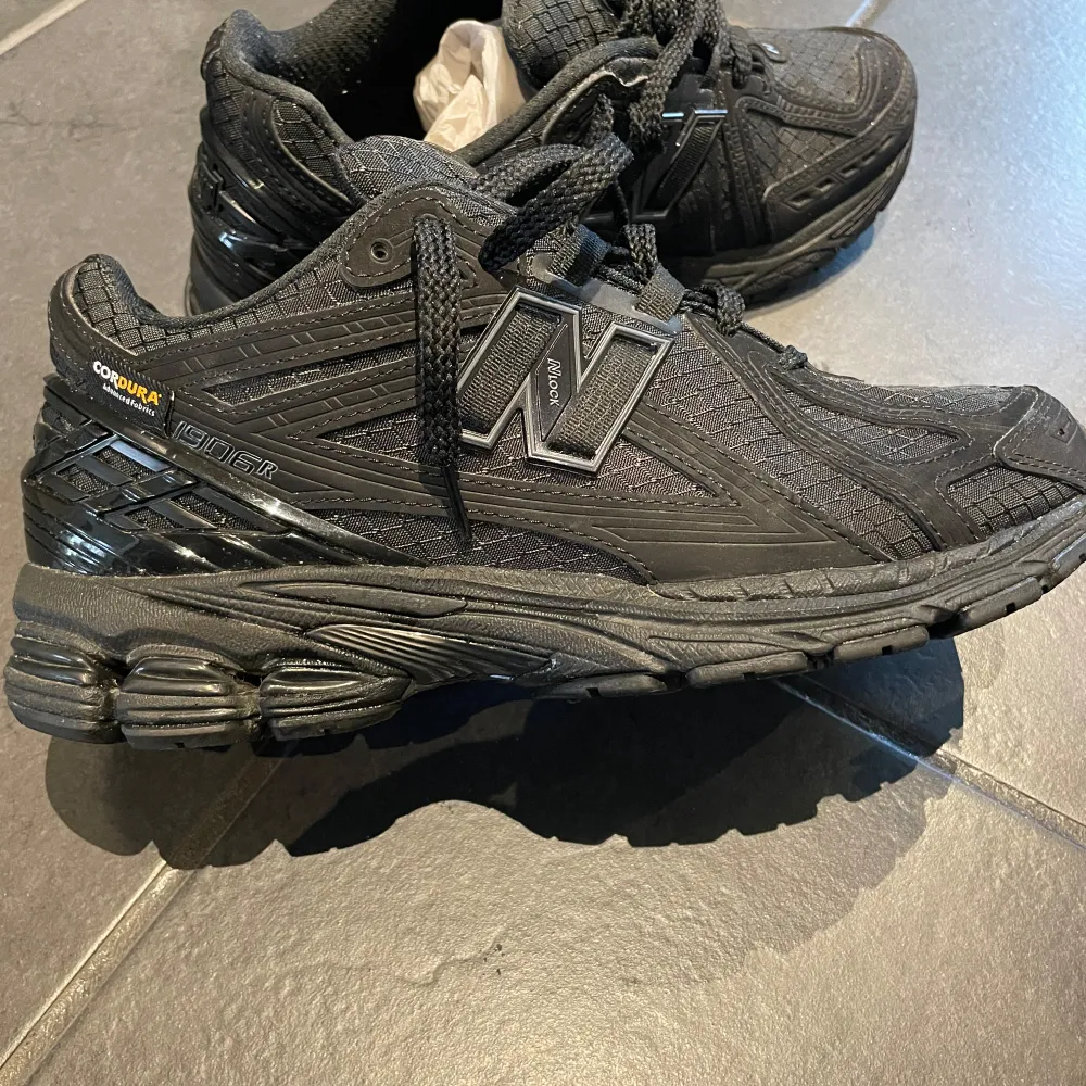 Snygga svarta sneakers från New Balance med robust design och Cordura-material för extra hållbarhet. Skorna har en rund tå och snörning för bra passform. Perfekta för både vardag och träning.. Kengät.