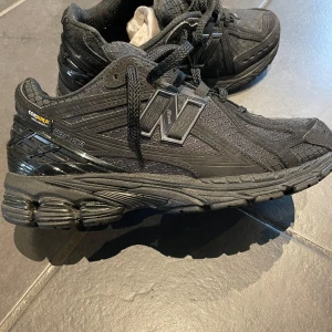 Svarta New Balance 1906R - Snygga svarta sneakers från New Balance med robust design och Cordura-material för extra hållbarhet. Skorna har en rund tå och snörning för bra passform. Perfekta för både vardag och träning.