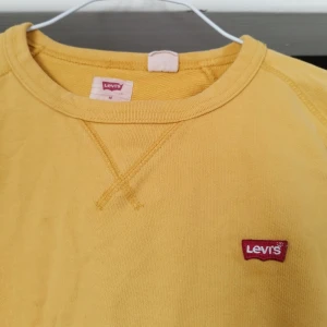 Gul långärmad tröja från Levi's - Säljer en gul långärmad tröja från Levi's med rund halsringning och ett litet rött Levi's-märke på bröstet. Perfekt för en avslappnad stil. Tröjan har en enkel och stilren design. Köpt på second hand, men i fint skick.