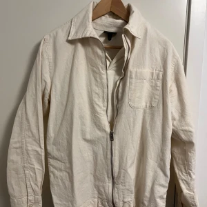 Vit jacka från Selected Homme - Säljer en stilren vit jacka från Selected Homme. Jackan har en dragkedja framtill och en bröstficka. Perfekt för en clean sommarkväll 