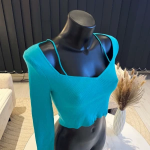 Turkos ribbad croppad topp - Snygg turkos ribbad topp med en unik design som kombinerar en lång ärm och en ärmlös sida. Toppen är croppad och har smala axelband på ena sidan. Perfekt för en trendig look. Passar perfekt i s/m storlek. Jag rekommenderar den varmt.🌸👌