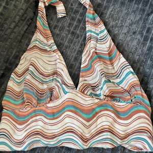 Mönstrad halterneck-topp från Pull&bear  - Säljer en Färgglad halterneck-topp med ett vågigt mönster i olika nyanser av brunt, orange, turkos och vitt. Toppen knyts runt nacken och ryggen, vilket ger en justerbar passform.                  Storlek: M