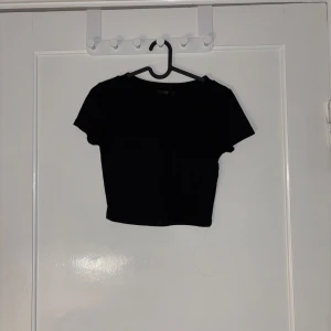 Svart croppad topp - Säljer en stilren svart croppad topp med korta ärmar. Perfekt för en trendig look och kan matchas med olika outfits. Ett måste i garderoben för den modeintresserade!