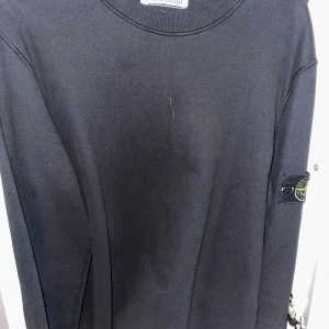 Svart Stone Island Crewneck - Säljer en stilren svart tröja från Stone Island. Tröjan har en rund halsringning och en ikonisk logotyp på ärmen. Perfekt för en casual look. Skick 9/10 knappt använd