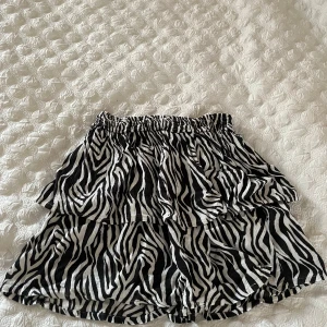 Zebramönstrad kjol från KappAhl - Snygg zebramönstrad kjol från KappAhl med volanger. Perfekt för att sticka ut med sin svartvita design. Elastisk midja för bekväm passform. 🦓✨