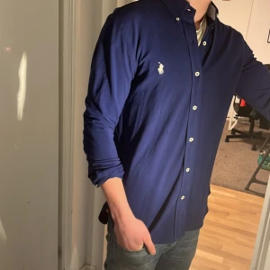 Ralph Lauren Skjorta - Tja säljer en Ralph lauren skjorta i färgen marinblå och i storlek S passar 170-180 cm ungefär. Nypris 1595 KR mitt pris 500 KR. Inga defekter som hål eller fläckar. Skriv vid frågor eller funderingar.