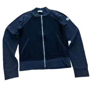 Svart  jacka från Moncler - Snygg mörkblå jacka från Moncler med dragkedja framtill och två praktiska fickor. Jackan har långa ärmar och ett stilrent märke på ärmen. Perfekt för en casual look. Ny pris≈3000kr mitt pris 1500kr