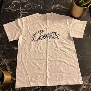 Corteiz tee - Säljer en vit t-shirt med ett coolt tryck i svart på framsidan. T-shirten är kortärmad och gjord av bomull, perfekt för en avslappnad stil. Passar bra till jeans eller shorts!