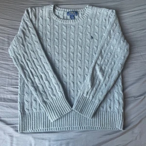 Polo Ralph Lauren Kabelstickad Tröja -  Polo Ralph Lauren Kabelstickad Tröja  Storlek: Junior L (14-16)  Skick: Utmärkt skick  Denna kabelstickade tröja från Polo Ralph Lauren är ett stiligt och mångsidigt tillskott till varje juniorgarderob. I en snygg grå färg är den i utmärkt skick och visar upp sitt kvalitativa hantverk och tidlösa design. Mått kan ges vid förfrågan.  ✅ Äkthet garanterad  📩 Öppen för rimliga erbjudanden - skicka ett meddelande om du har några frågor.  🚚 Frakt - skickas samma dag eller inom 24 timmar