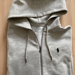Grå hoodie från Polo Ralph Lauren - Säljer en stilren grå hoodie från Polo Ralph Lauren. Storlek Xs. Säljer för 900kr. Priset kan diskuteras något. Det finns ett jättelitet hål på bakre ärm på höger sida.