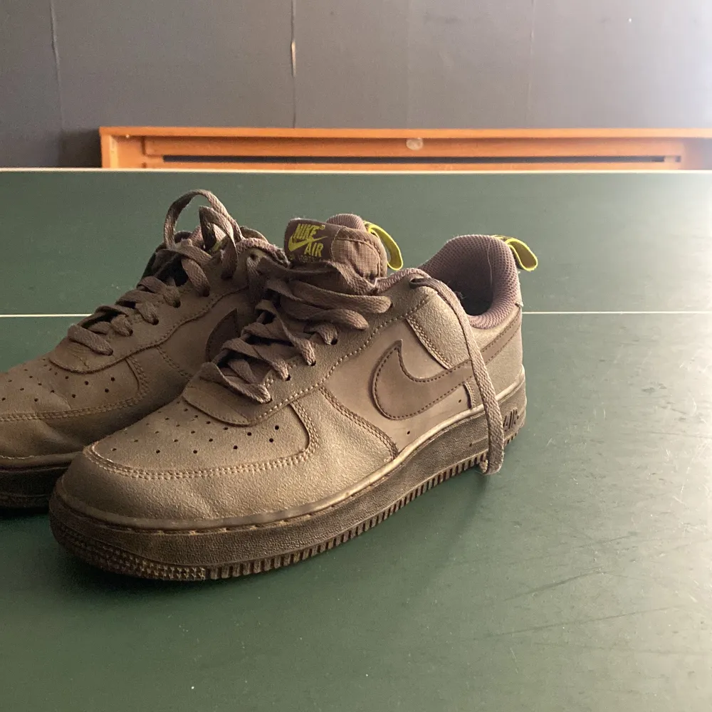 Säljer ett par bruna Nike Air Force 1 med snörning och limegröna detaljer. Skorna har en klassisk rund tå och är perfekta för en avslappnad stil. Tyvärr finns de inte box eller kvitto. Kengät.