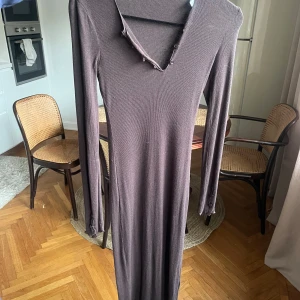 Brun långklänning från Samsøe Samsøe - Snygg brun långklänning från Samsøe Samsøe i ribbat material. Klänningen har långa ärmar och en v-ringad hals med knappar. Perfekt för en stilren look. Aldrig använd nypris 1.700