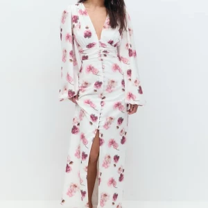 Vit blommig långklänning - Elegant vit långklänning med rosa blommönster och djup v-ringning. Klänningen har långa ärmar och en slits framtill som ger en stilfull touch. Perfekt för sommarens festligheter.