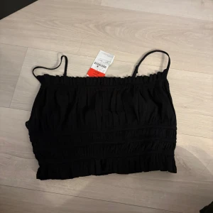 Svart linnetopp från Stradivarius - Säljer en stilren svart linnetopp från Stradivarius med smala axelband och rynkad design. Perfekt för varma dagar eller som ett lager under en jacka. Toppen har en elastisk kant för en bekväm passform.