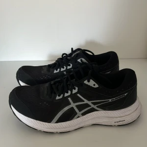 Svarta löparskor från Asics - Säljer ett par svarta löparskor från Asics med vita detaljer och snörning. Skorna har en bekväm sula med AmpliFoam-teknologi och Ortholite-inlägg för extra komfort. Perfekta för löpning och träning.