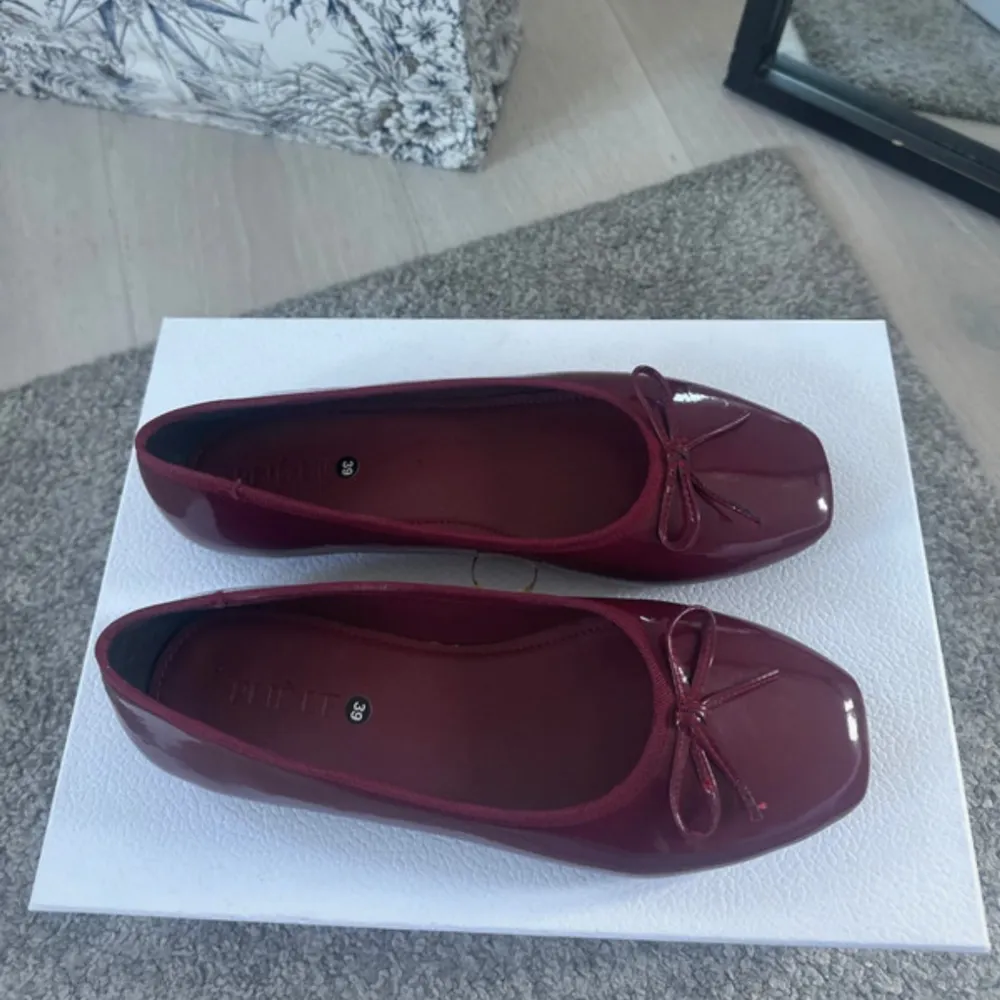 Eleganta vinröda ballerinaskor med en söt rosett på ovansidan. Skorna har en glansig finish och en rund tå, vilket ger dem en klassisk look. Perfekta för att lägga till en touch av färg till din outfit.. Kengät.