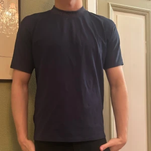 Mörkblå Acne t-shirt - Säljer en stilren mörkblå Acne t-shirt med normal passform. Perfekt för en avslappnad look. Kortärmad och tillverkad i ett mjukt material för extra komfort. Modellen är 183.
