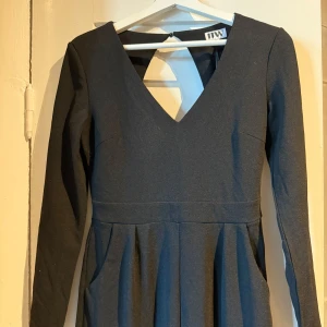 Svart långärmad byxdress med öppen rygg – stl M -   Elegant och stilren svart byxdress med lång ärm och djup v-ringning både fram och bak. Fin passform med markerad midja och fickor. Dragkedja bak och knapp i nacken.  Perfekt till fest, dejtkväll eller event! Tyg med lite stretch – sitter snyggt på kroppen. Använd 1 gång, mycket fint skick.  Storlek: M (passar även S beroende på önskad passform)