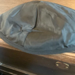 Svart kippa - Säljer en svart ögonmask i syntetmaterial. Perfekt för att blockera ljus och få en god natts sömn. Enkel och bekväm design.