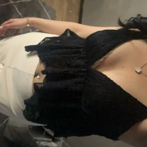 Svart topp med volangdetaljer - Snygg svart topp med volangdetaljer och djup v-ringning. Perfekt för en kväll ute eller en speciell tillställning. Toppen har en elegant och feminin stil.