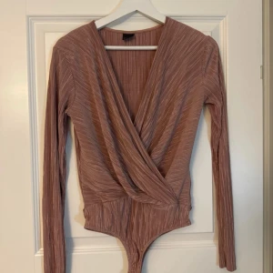 Rosa omlott body från Gina Tricot - Säljer en snygg rosa omlott body från Gina Tricot. Den har långa ärmar och ett ribbat mönster som ger en stilren look. Perfekt för att styla med både jeans och kjol. 💖