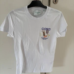Vit t-shirt från Casablanca - Snygg vit t-shirt från Casablanca med färgglatt tryck av tennisutrustning och texten 'casa' och 'Équipement Sportif'. Sorlek S. Som ny