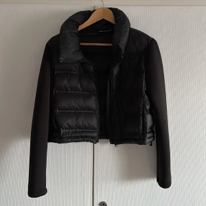 Svart pufferjacka från Zara - Snygg svart pufferjacka från Zara med dragkedja framtill. Jackan har långa ärmar och en hög krage för extra värme. Perfekt för kyliga dagar när du vill hålla stilen.