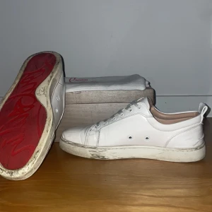 Vita sneakers från Christian Louboutin - Snygga vita sneakers från Christian Louboutin med den ikoniska röda sulan. Skorna har en klassisk design med snörning och rund tå. Perfekta för en stilren look. Dustbag och kvitto samt skolådan kommer med. 