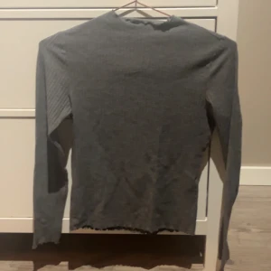 Grå ribbad tröja - Säljer en stilren grå ribbad tröja med långärmad design. Perfekt för lager-på-lager under kyligare dagar. Enkel och mångsidig för olika outfits.
